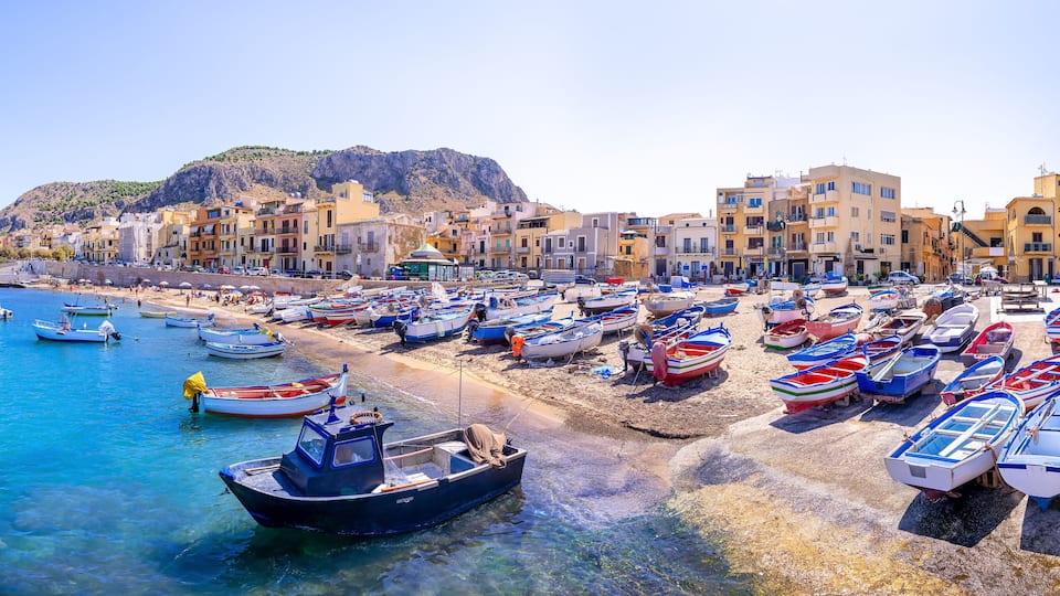 A coastal town with colorful buildings, a beach, and numerous small boats.