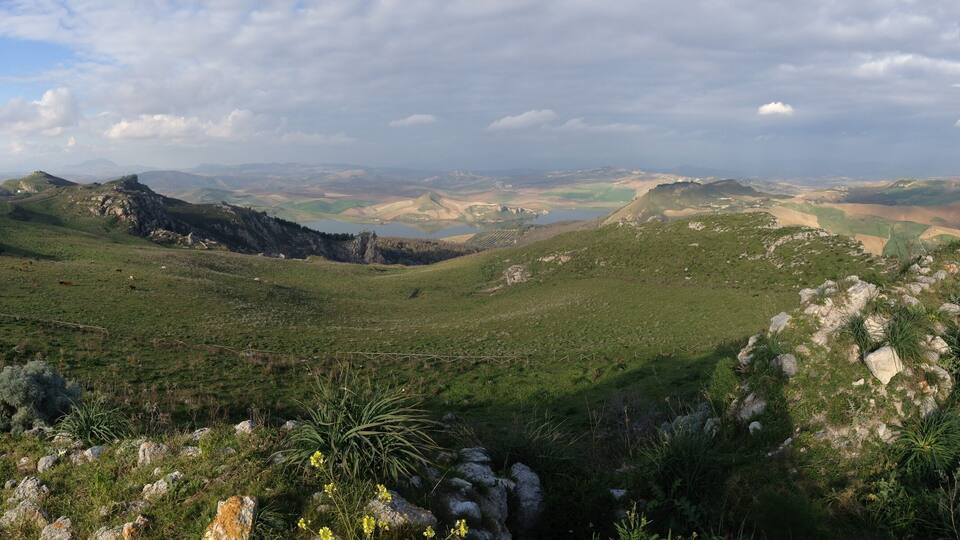 A mountainous landscape with green valleys, rocky outcrops, and a winding road.