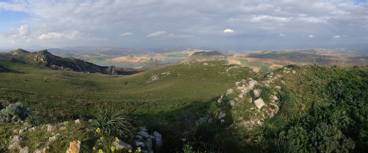 A mountainous landscape with green valleys, rocky outcrops, and a winding road.