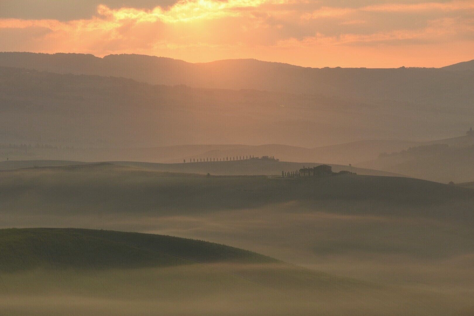 Rolling hills, a misty valley, and a distant structure silhouetted against the sun.