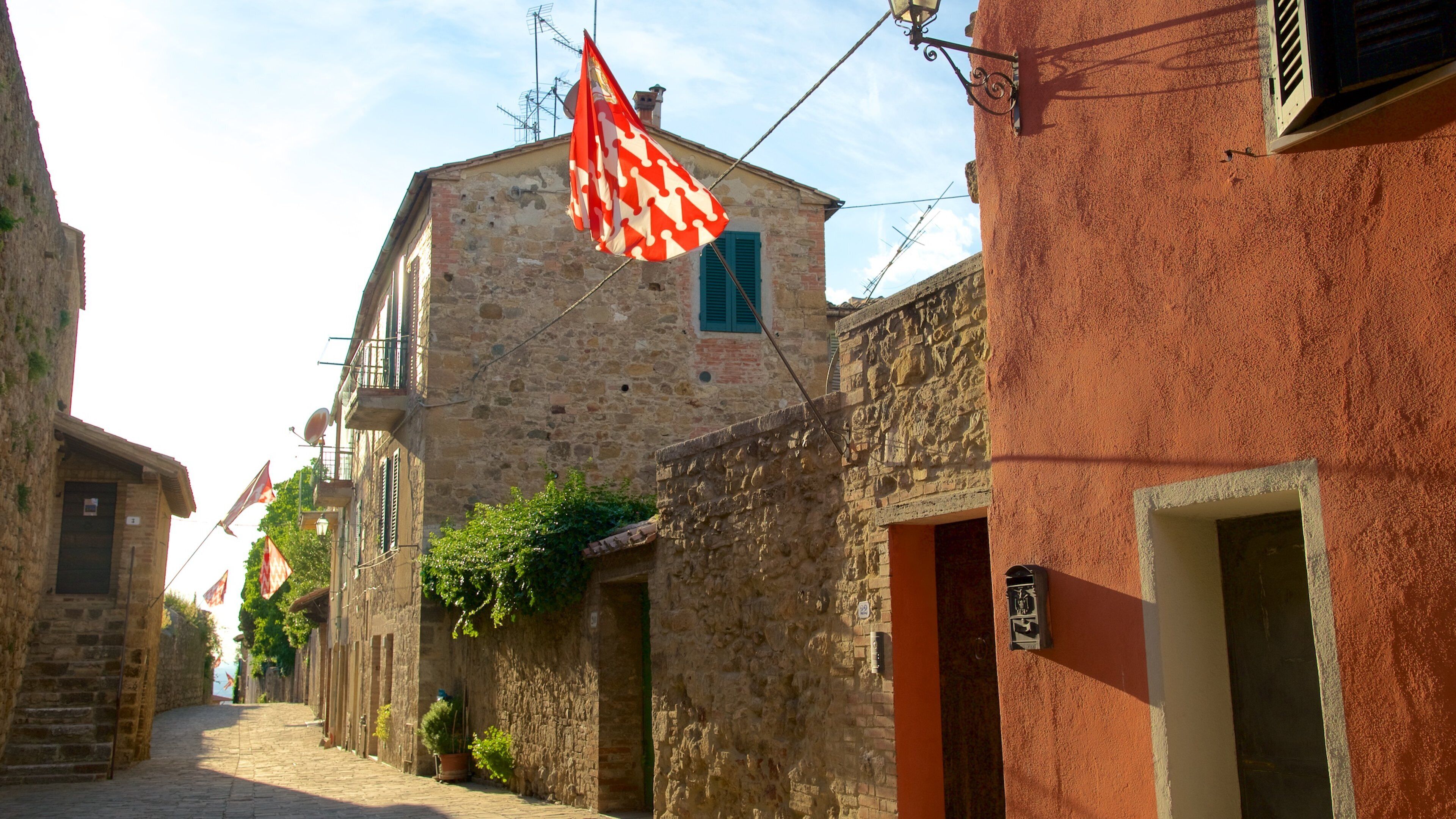 A narrow cobblestone street lined with historic stone buildings, some with green shutters and ivy.