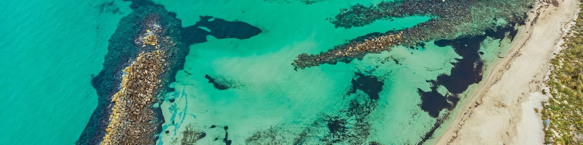 A coastal landscape with clear turquoise waters, a rocky shoreline, and sandy beach areas.