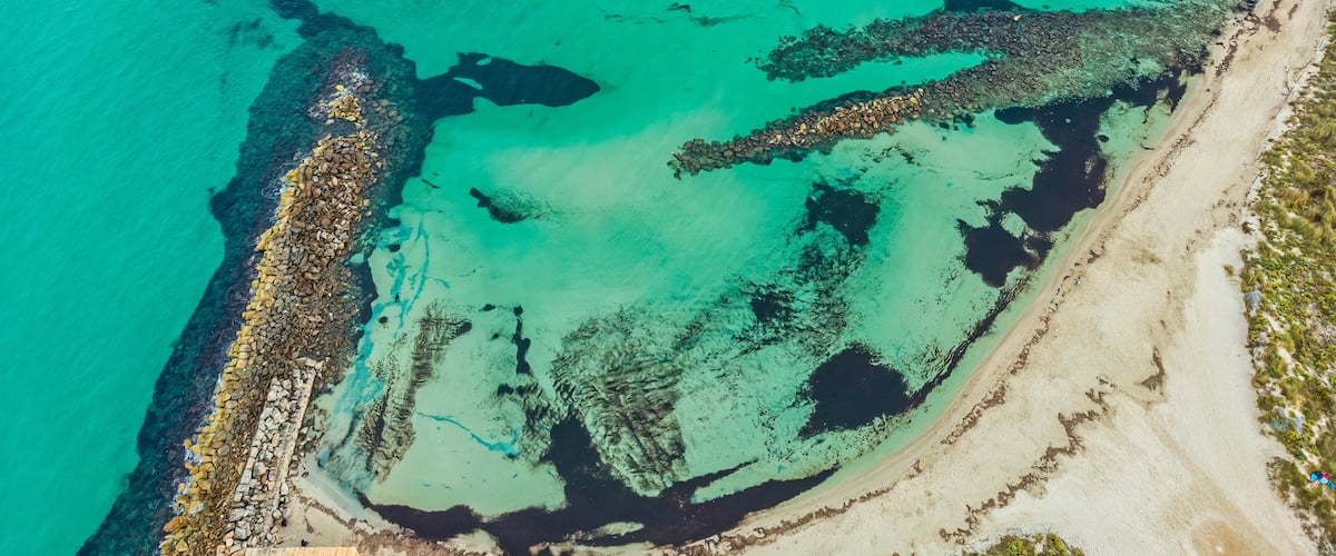Un paisaje costero con aguas turquesas cristalinas, una costa rocosa y zonas de playa arenosa.