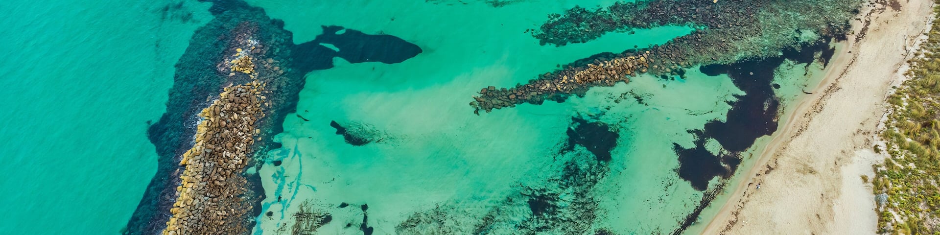 A coastal landscape with clear turquoise waters, a rocky shoreline, and sandy beach areas.