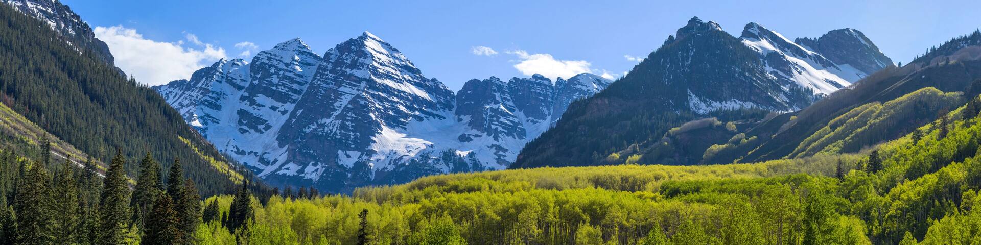 Maroon Bells - A panoramic view of Maroon Bells rising high in lush green Maroon Creek Valley, as seen from side of Maroon Creek Road, on a sunny Spring evening. Aspen, Colorado, USA.