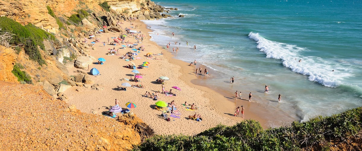 Una playa con gente, sombrillas y acantilados rocosos.