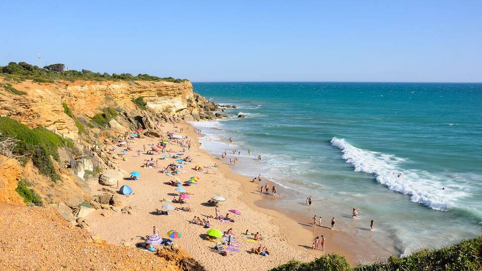 A beach with people, umbrellas, and rocky cliffs.