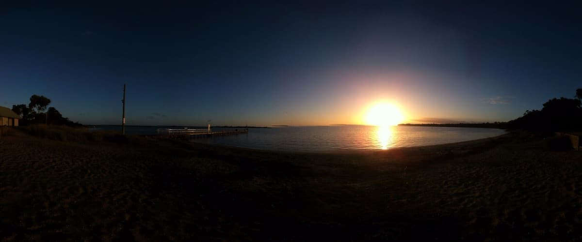 A sunset over a calm body of water with a pier extending into the water.
