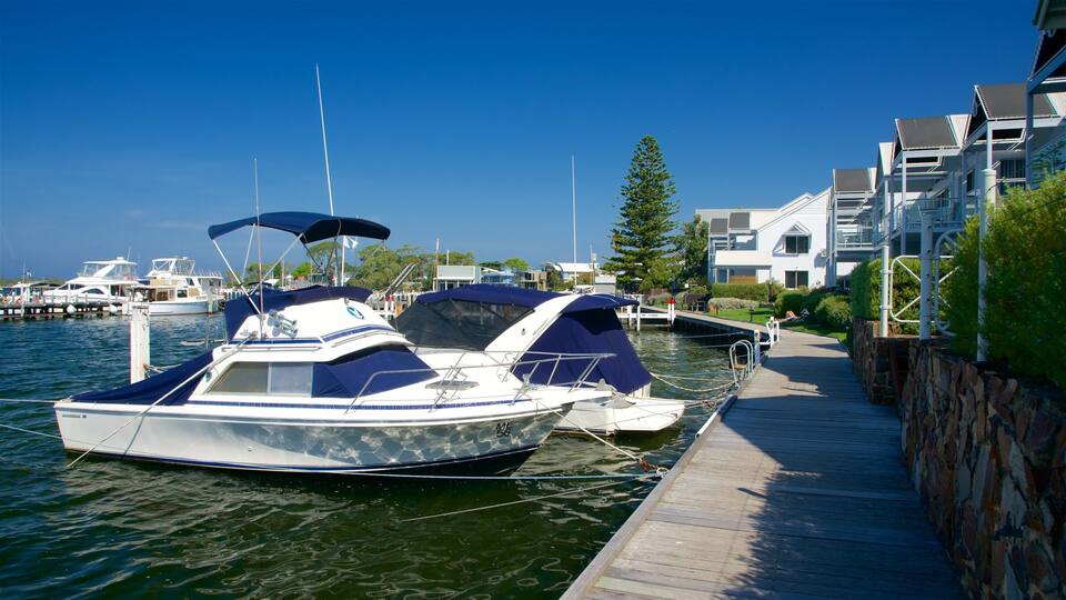 A marina with boats docked, a wooden walkway, and modern buildings in the background.