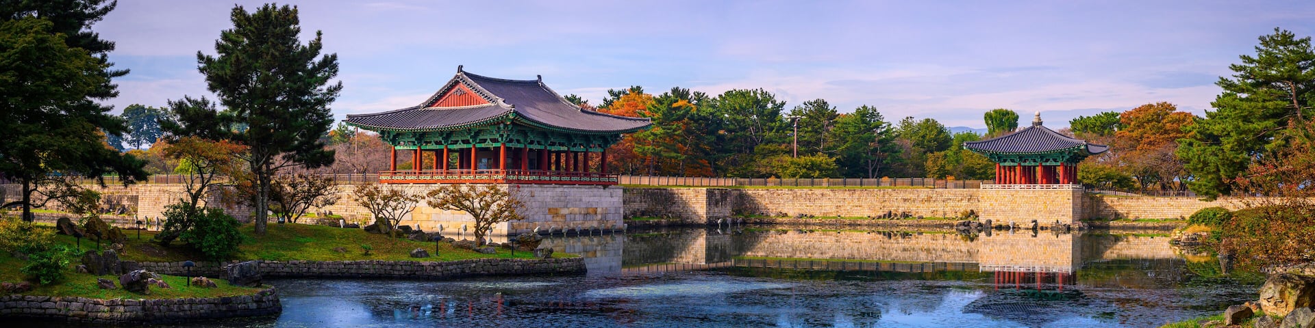 Traditional Korean architecture with a pond and autumn foliage.