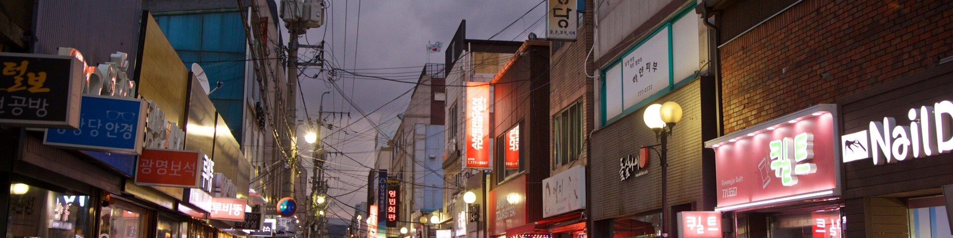 Una estrecha calle urbana bordeada de comercios y vehículos estacionados.