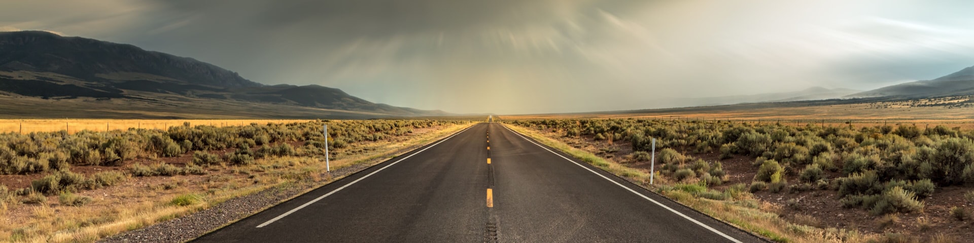 Long straight road in Utah with dramatic clouds and rain rolling in