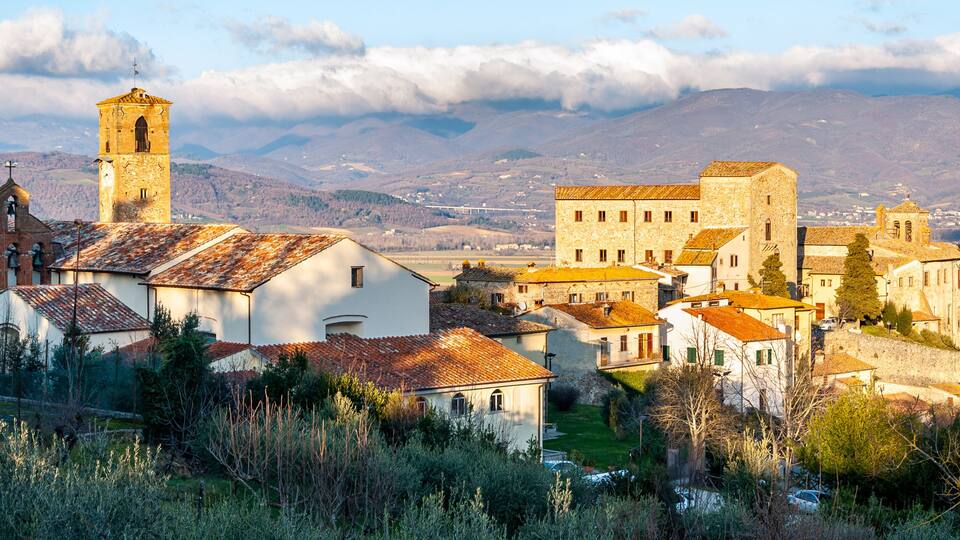 A historic town with a prominent church tower, stone buildings, and a mountainous backdrop.