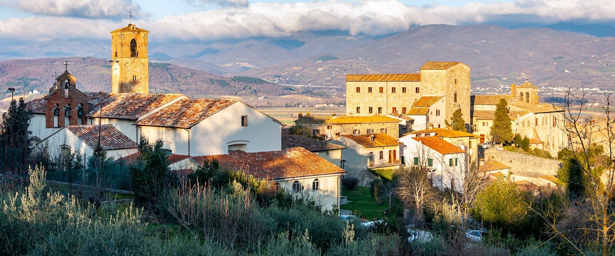A historic town with a prominent church tower, stone buildings, and a mountainous backdrop.