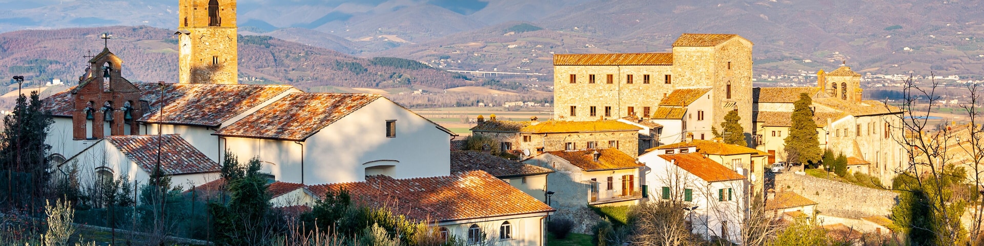 A historic town with a prominent church tower, stone buildings, and a mountainous backdrop.