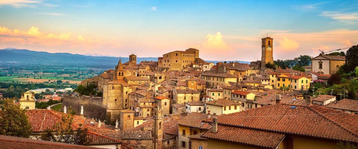 Un poble antic amb edificis de teules de terracota, una església destacada i una serralada de muntanyes al lluny.