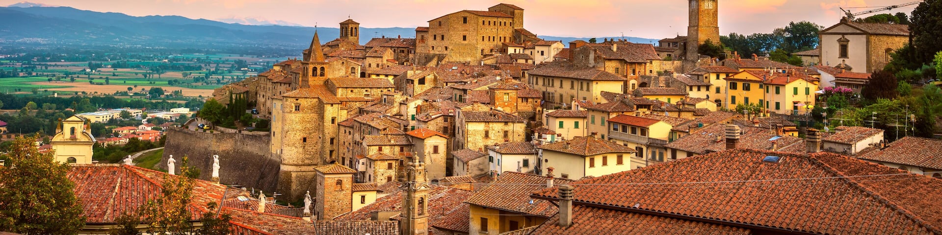 A historic town with terracotta-roofed buildings, a prominent church, and a distant mountain range.