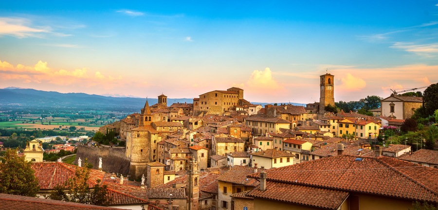 A historic town with terracotta-roofed buildings, a prominent church, and a distant mountain range.