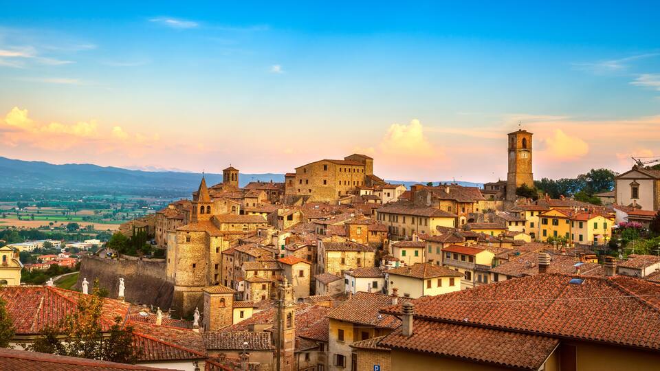 A historic town with terracotta-roofed buildings, a prominent church, and a distant mountain range.