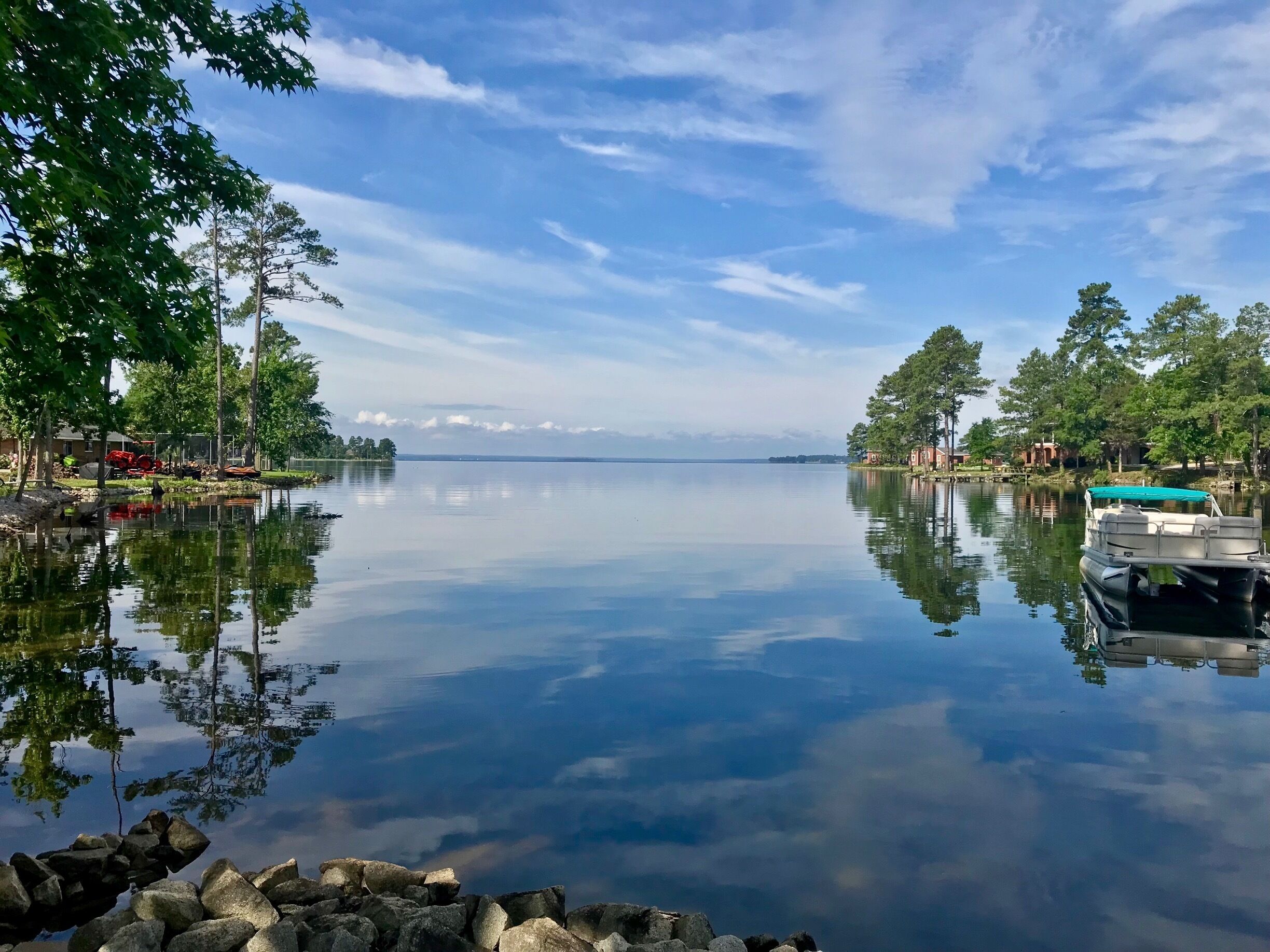 A calm lake with a boat docked on the right, surrounded by trees and buildings.