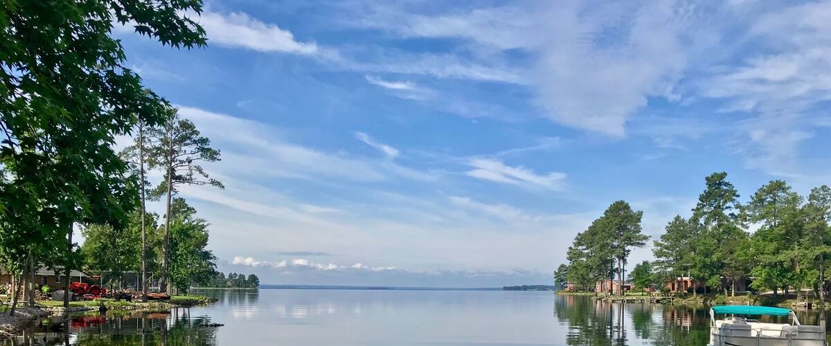 A calm lake with a boat docked on the right, surrounded by trees and buildings.