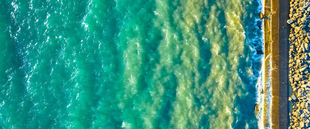 A coastal area with turquoise waters, a rocky shoreline, and a paved walkway.