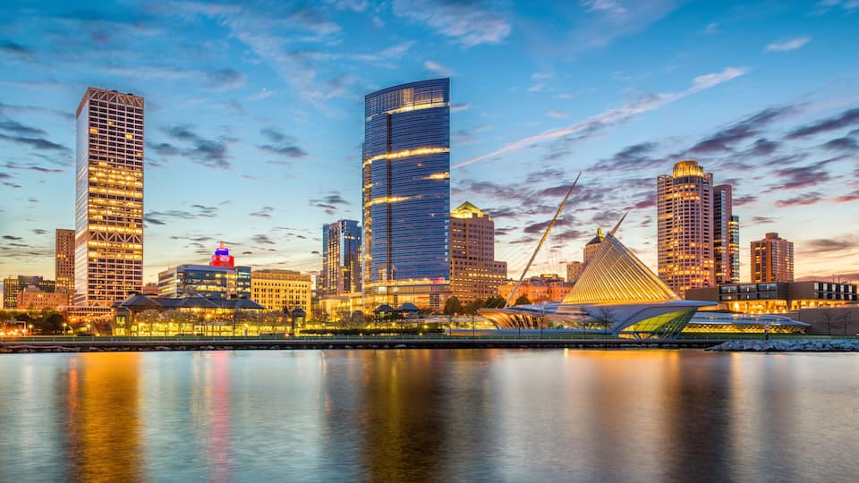 A city skyline with modern skyscrapers and a river in the foreground.