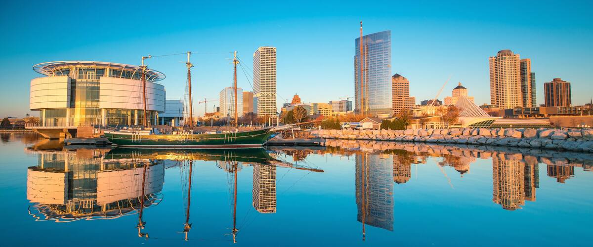 Milwaukee skyline at twilight with city reflection in lake Michigan and harbor pier.