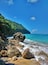 A rocky shoreline with clear turquoise water and a lush green cliff.
