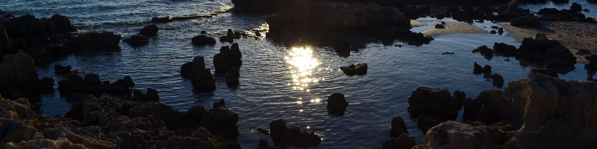 A rocky shoreline with the sun reflecting off the water.