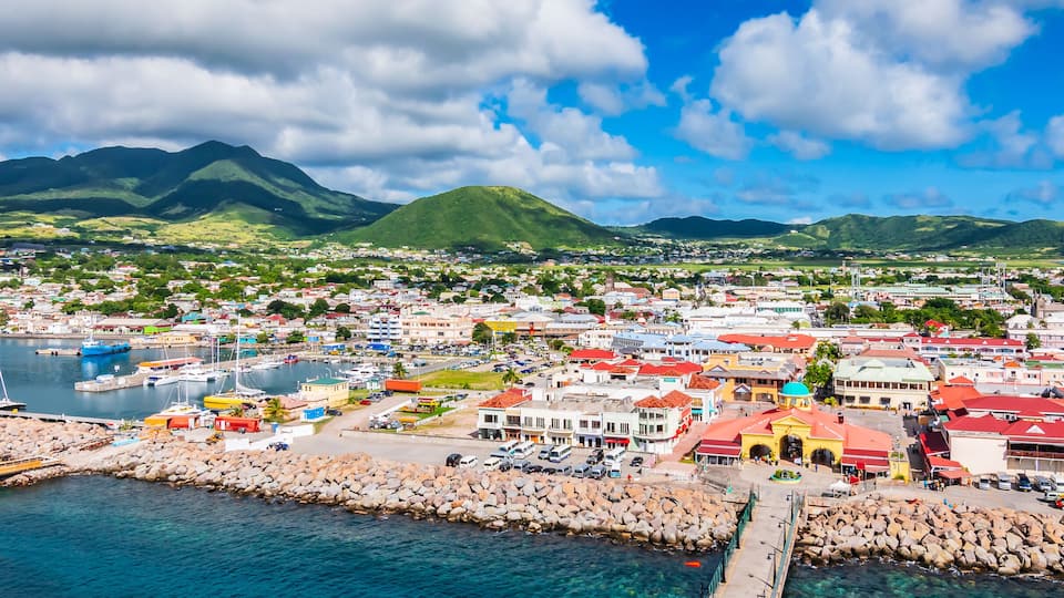 A coastal town with a marina, rocky breakwater, and mountainous backdrop.