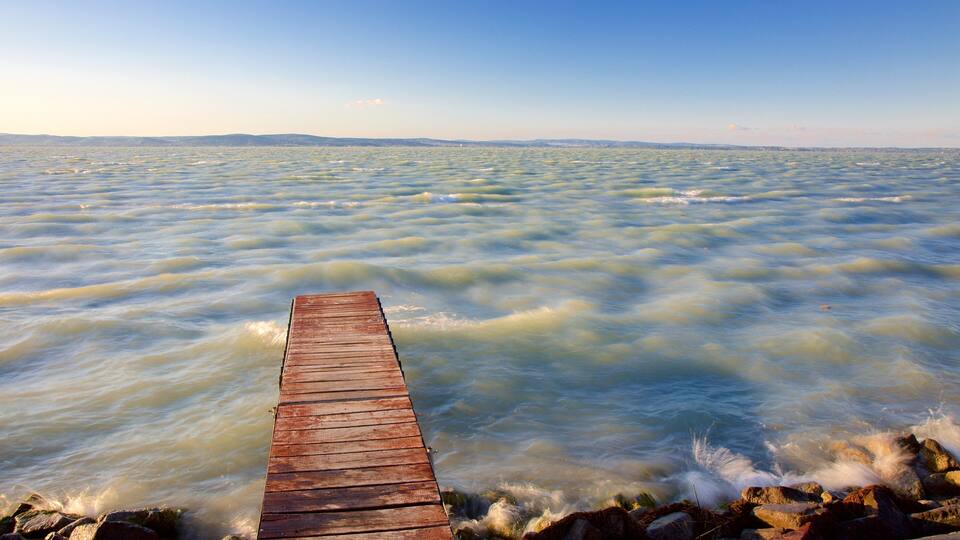 A wooden pier extending into a body of water with gentle waves and a clear sky.