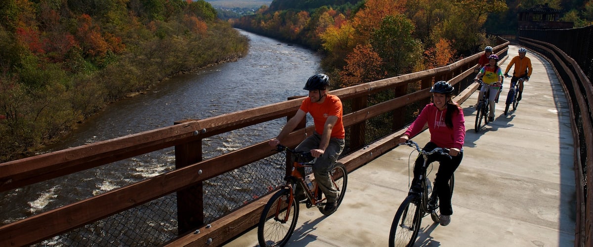 A group of cyclists on a bridge over a river surrounded by autumn foliage.