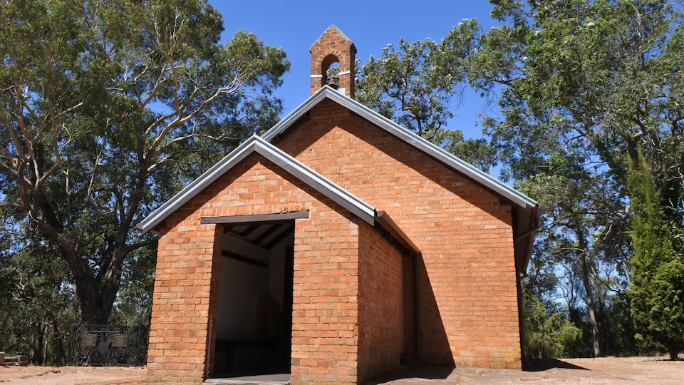 A small brick church with a bell tower, surrounded by trees.