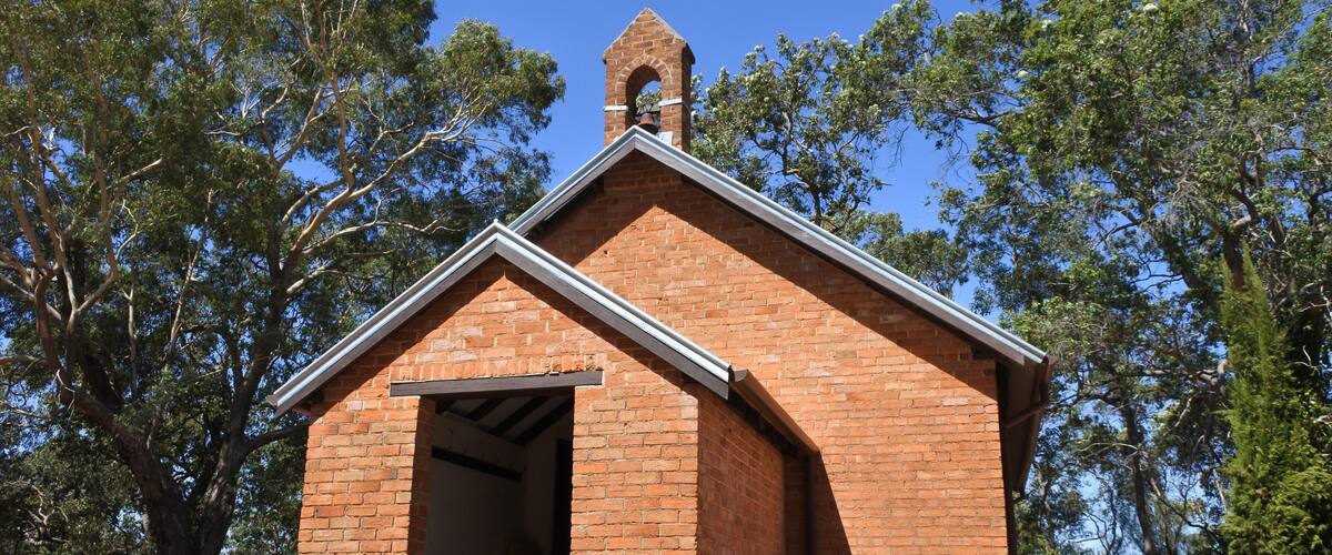 A small brick church with a bell tower, surrounded by trees.