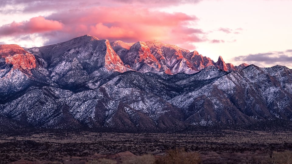 A mountain range with snow-covered peaks and a desert landscape in the foreground.