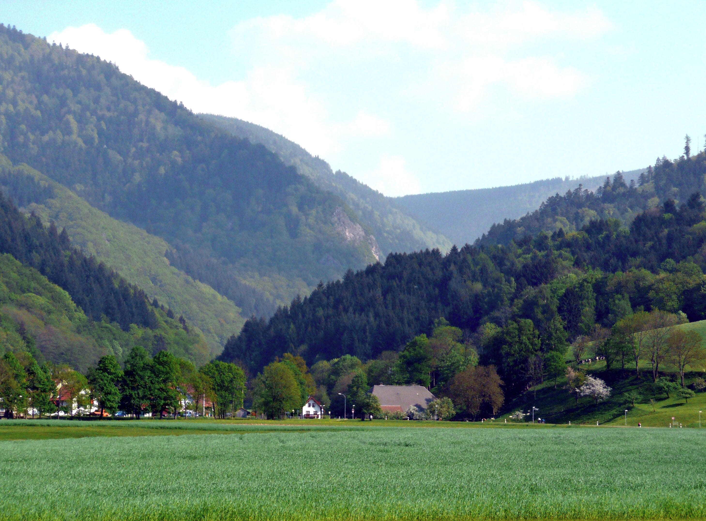 A valley with a field, a house, and forested hills.