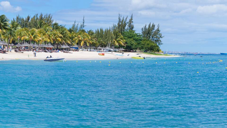 A beach with palm trees, a boat, and a large ship in the distance.