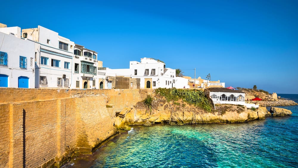 A coastal town with white buildings, clear blue waters, and a rocky shoreline.