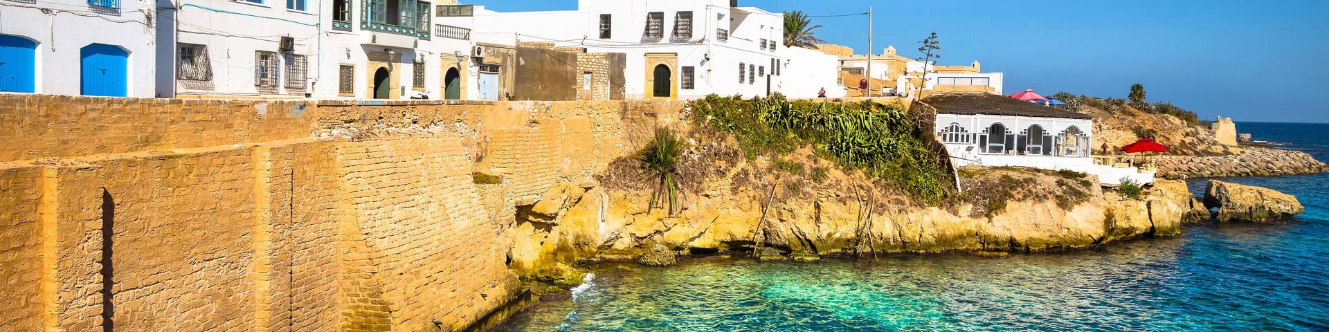 A coastal town with white buildings, clear blue waters, and a rocky shoreline.