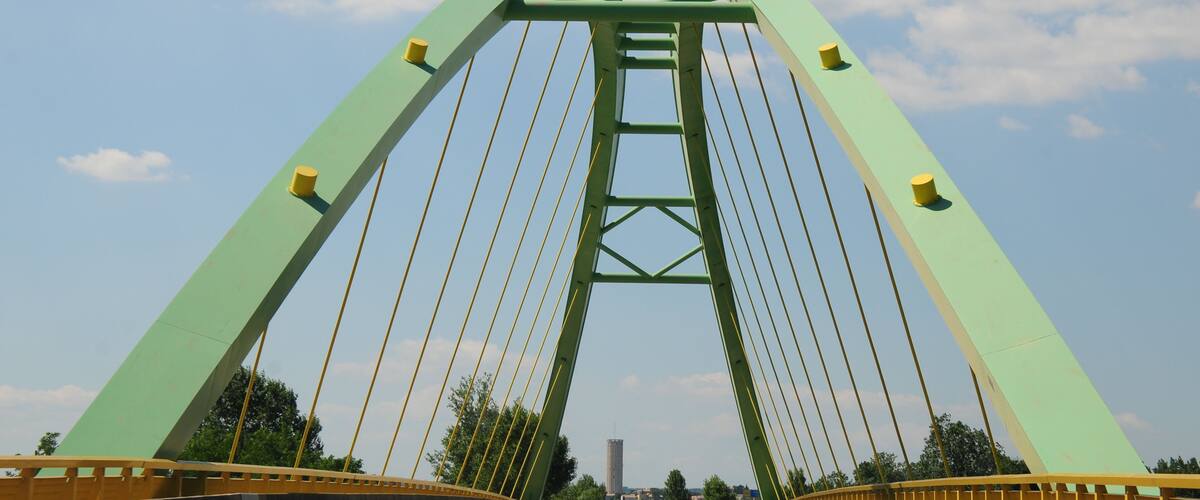 A green suspension bridge with yellow railings and cables.