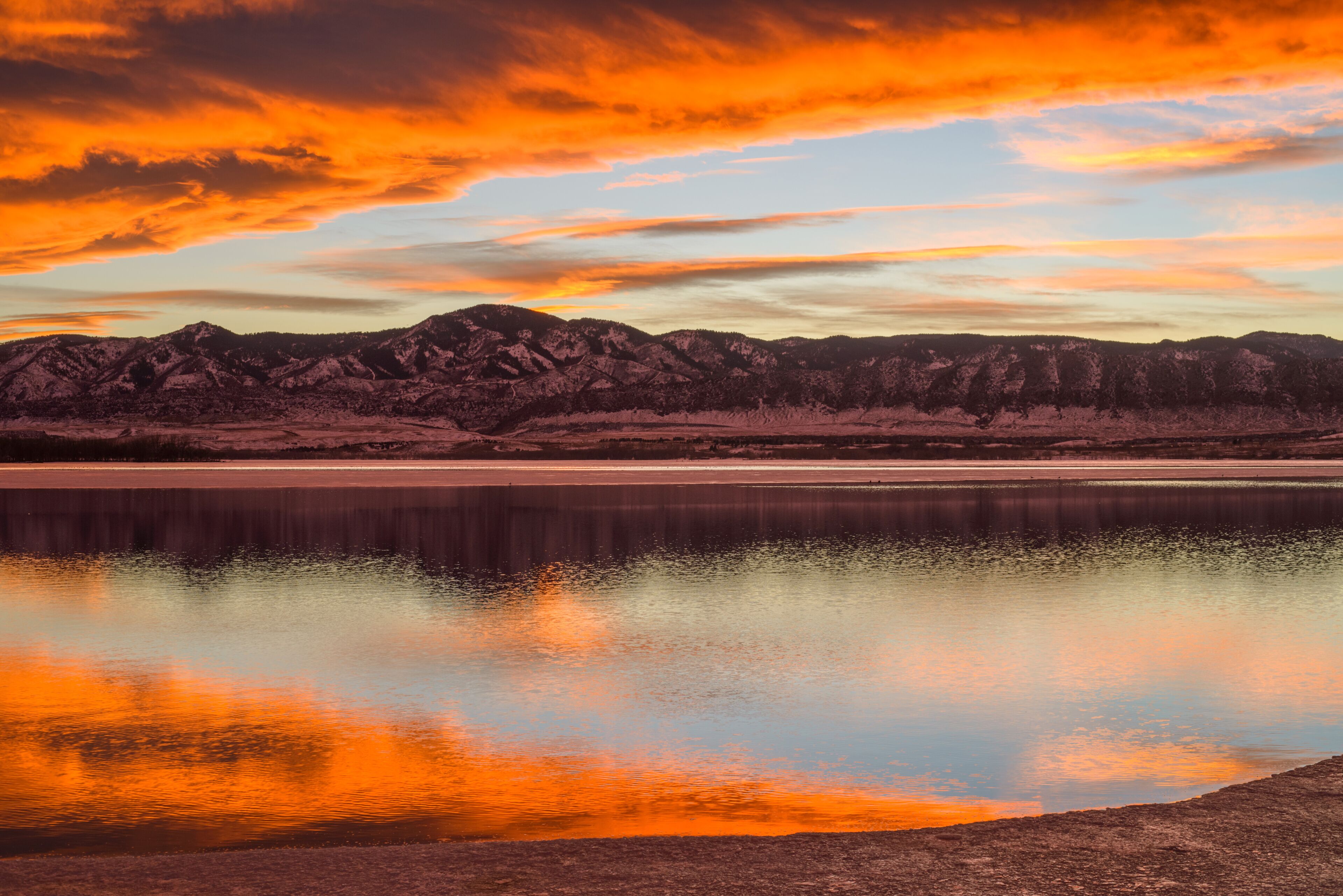 Sunset Spring Mountain Lake - Colorful stormy clouds rolling over a melting ice lake, with snow mountain range reflection, as spring sun sets.