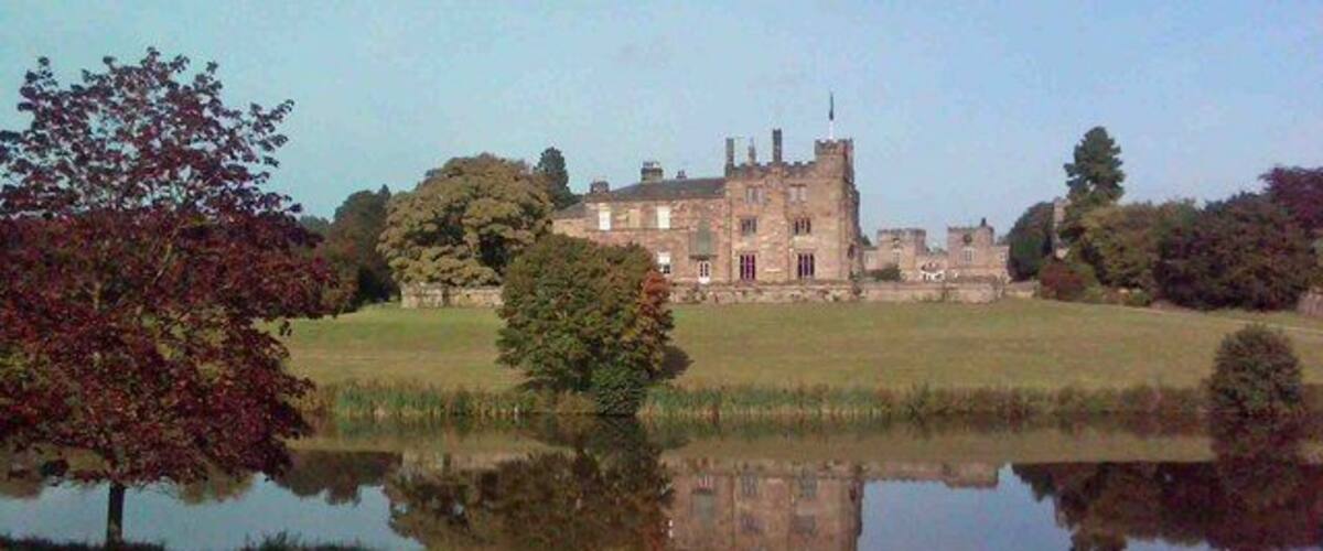 Un vaste domaine comprenant un étang, des arbres et, au loin, un bâtiment qui ressemble à un château.