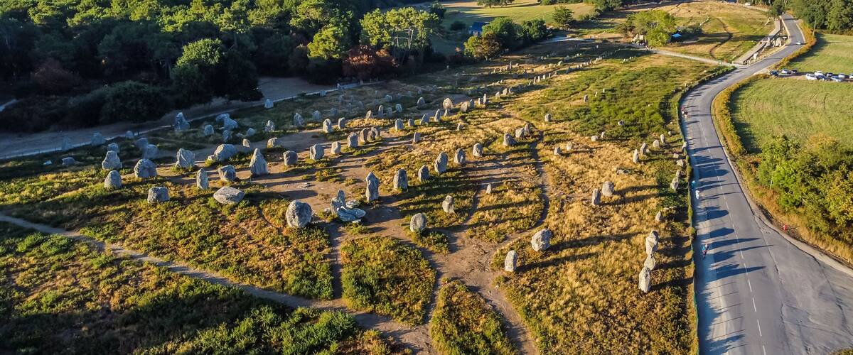 An aerial view of a landscape with a winding road, a field of standing stones, and dense forested areas.