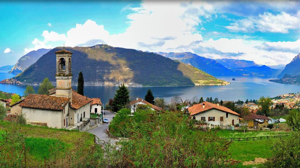 A church with a bell tower, a lake, and mountains in the background.