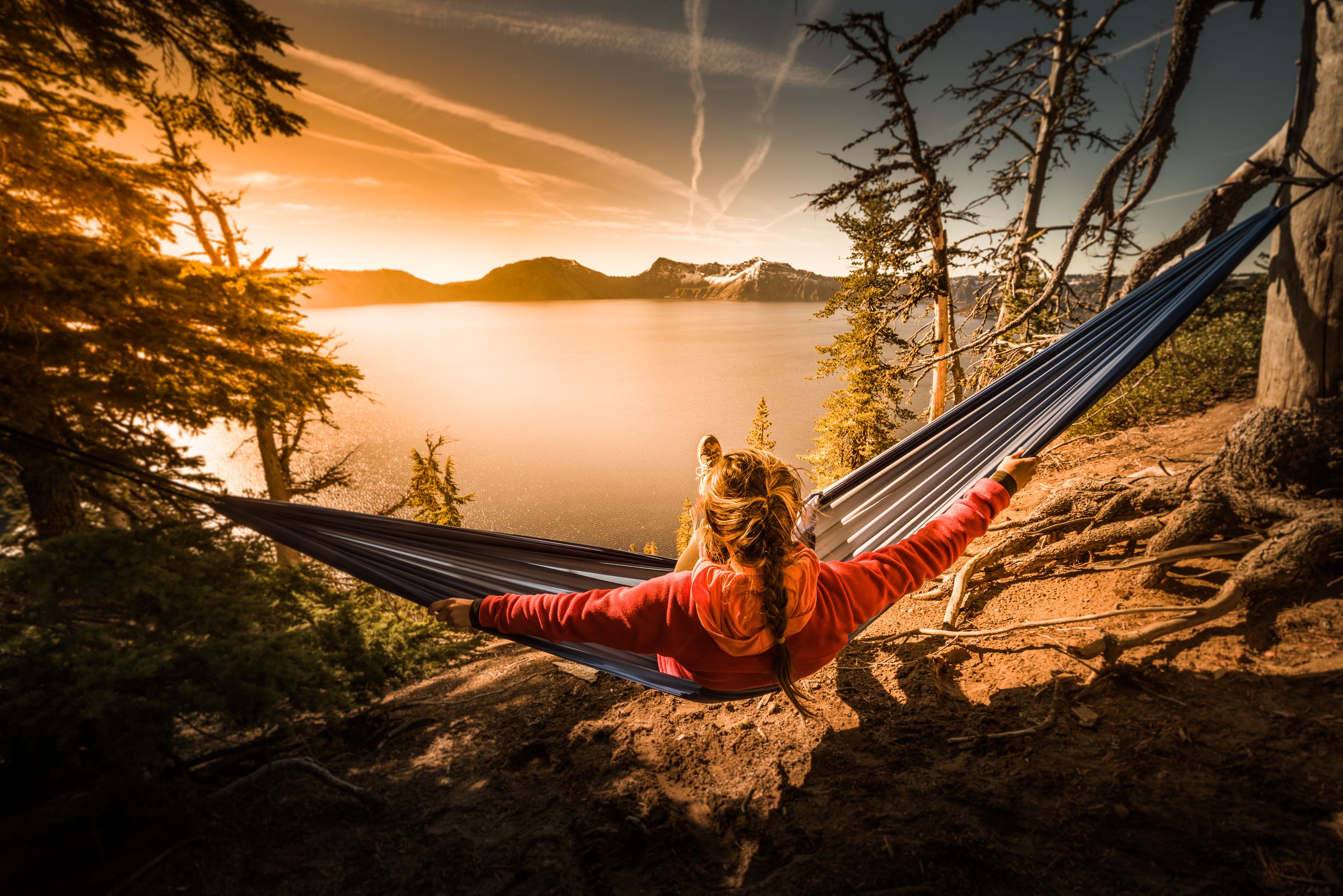 A person relaxing in a hammock overlooking a lake with mountains in the background.