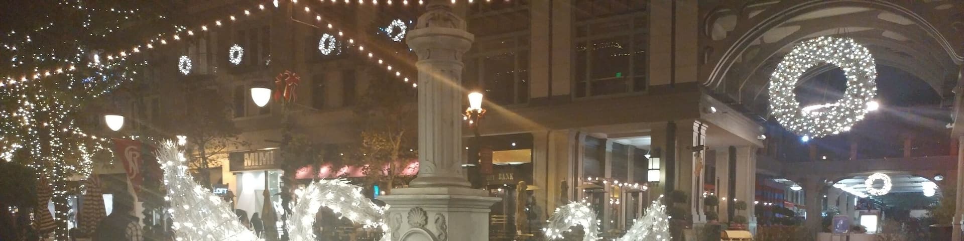 A fountain with water jets in a tiled planter surrounded by red poinsettia plants.