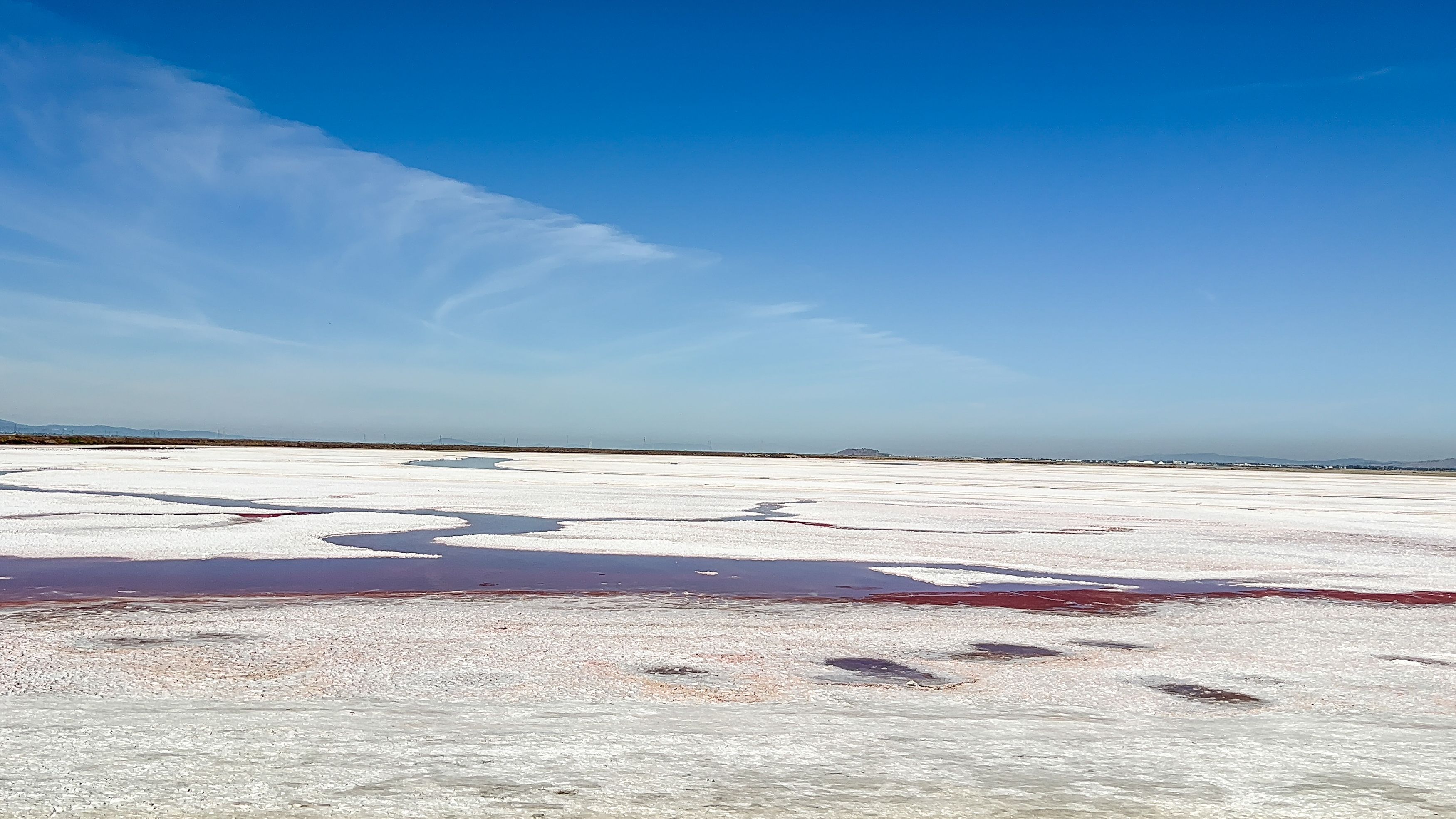 Una salina con depósitos de sal blanca y zonas rojas de sal bajo un cielo azul despejado.