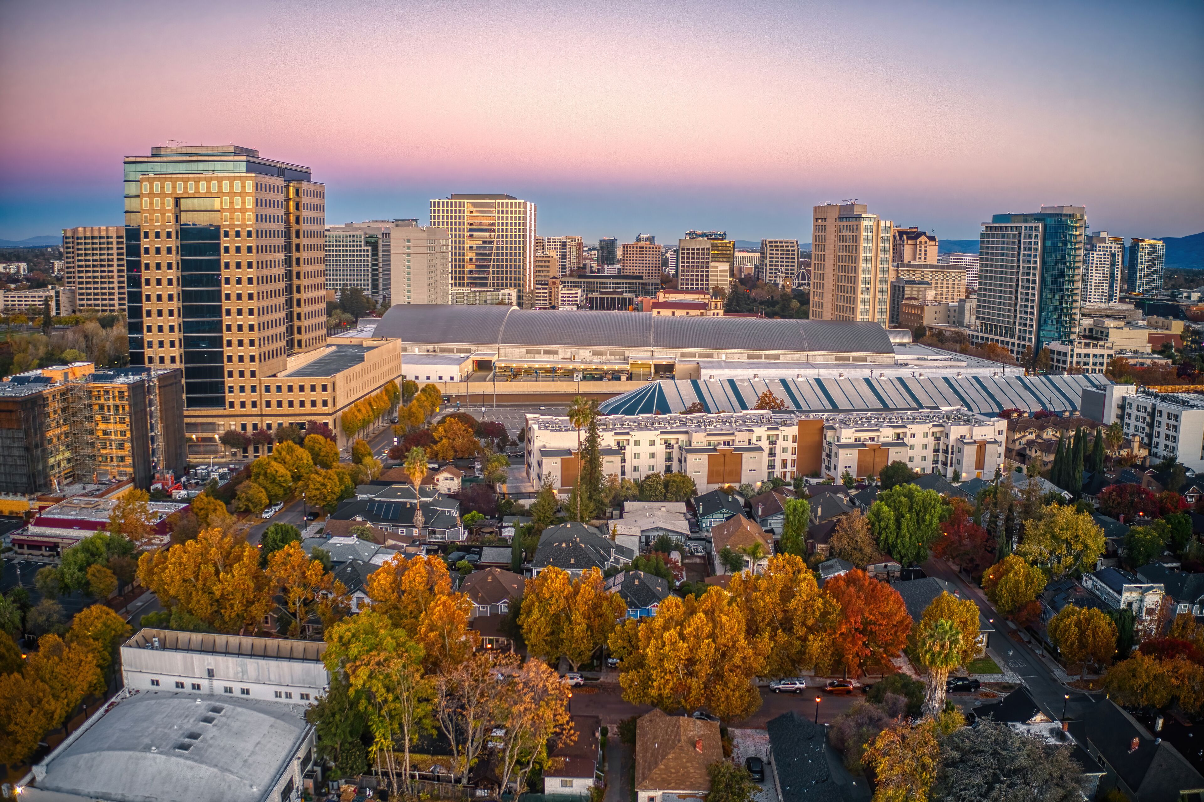 A cityscape with autumn-colored trees, a large stadium, and various high-rise buildings.