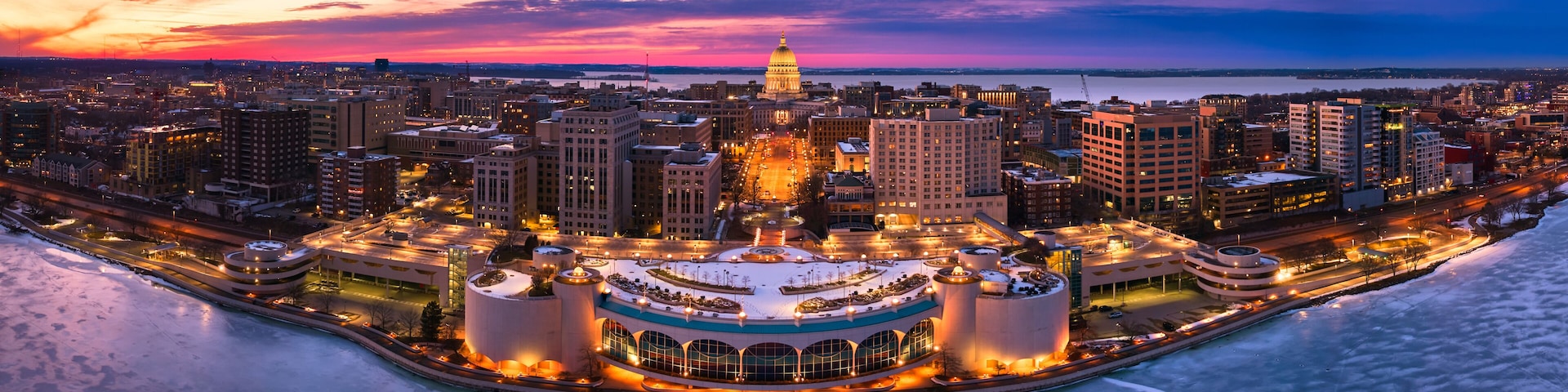 A cityscape at dusk with a prominent dome-shaped building, a waterfront, and a circular structure with multiple towers.